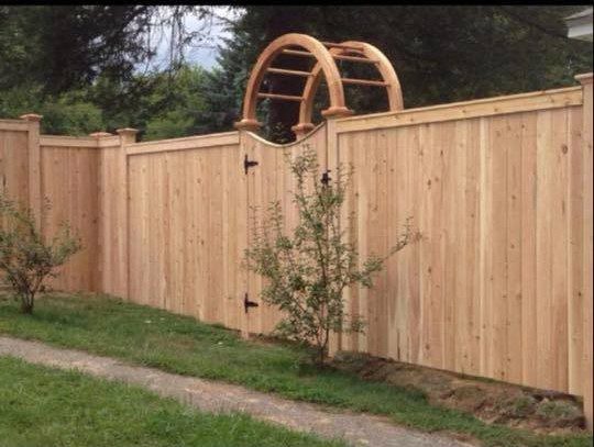 152765386_362082648297468_8704988294835131321_n Wooden fence with arched gate and plants.