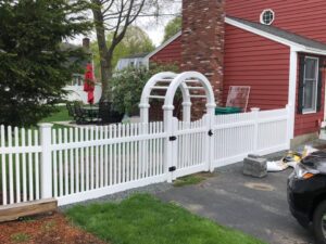 White fence and archway by red house.