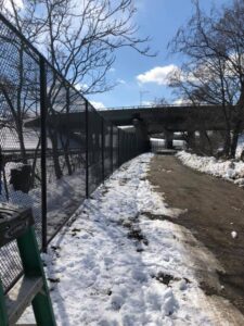 Snowy path beside fence and bridge.